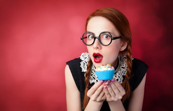 Κοκκινομάλλα κοπέλα με cupcake σε κόκκινο φόντο — Φωτογραφία Αρχείου