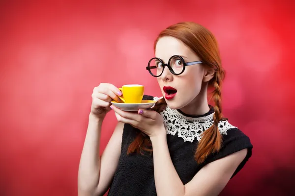 Руда дівчина чашкою ароматної кави на червоному тлі. — стокове фото