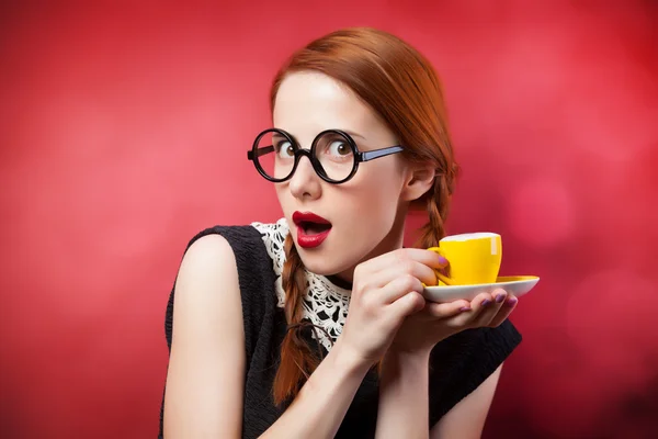 Roodharige meisje met kopje koffie op rode achtergrond. — Stockfoto