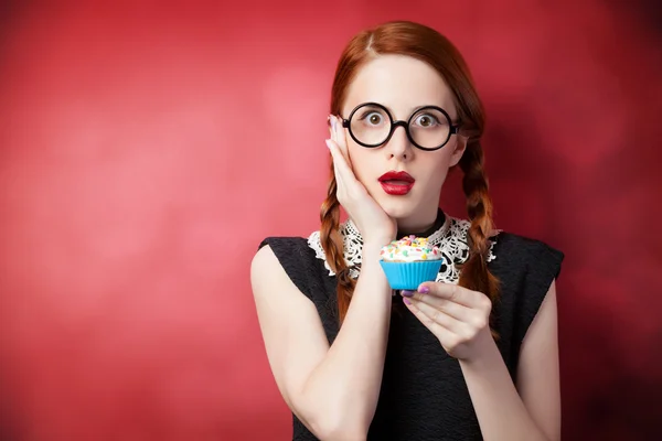 Roodharige meisje met cupcake op rode achtergrond — Stockfoto