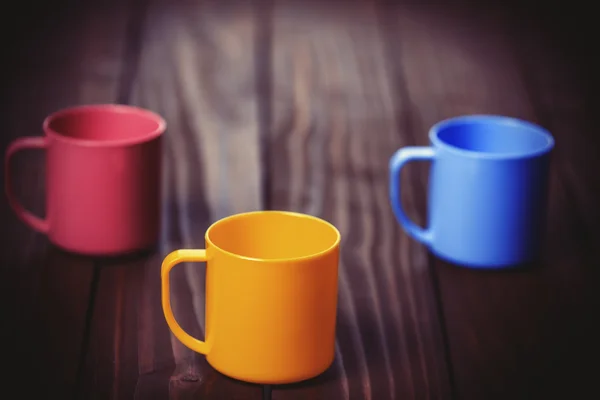 Drei farbige Tassen auf Holztisch. — Stockfoto