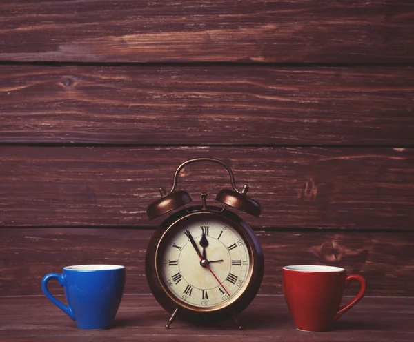 Zwei Teetassen und Alarmuhr auf Holztisch. — Stockfoto