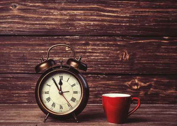 Taza de café y despertador en mesa de madera . — Foto de Stock