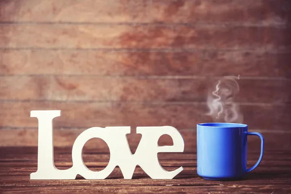 Φλιτζάνι τσάι ή καφέ με τη λέξη αγάπη στο woodent τραπέζι. — Φωτογραφία Αρχείου