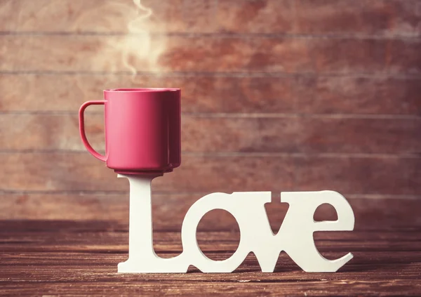 Φλιτζάνι τσάι ή καφέ με τη λέξη αγάπη στο woodent τραπέζι. — Φωτογραφία Αρχείου