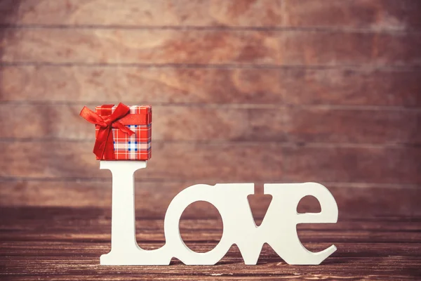 Mały prezent i słowo miłość na drewnianym stole. — Zdjęcie stockowe