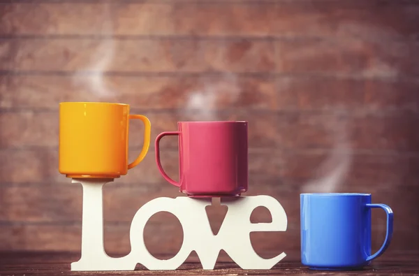 Drie kopjes koffie en word liefde op houten tafel. — Stockfoto