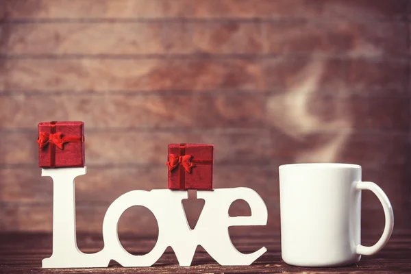 Cup of coffee, gift and word Love on wooden table. — Stock Photo, Image