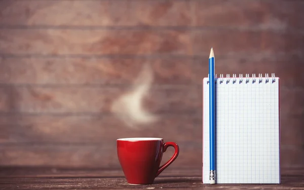 Kopp kaffe och anteckningsbok på trä bakgrund. — Stockfoto