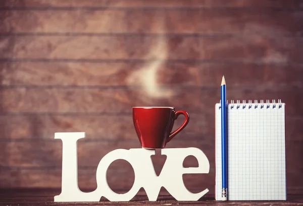 Tazza di caffè con parola Amore e taccuino su sfondo di legno . — Foto Stock