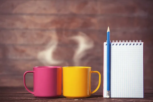 Twee kopjes koffie en notebook op houten achtergrond. — Stockfoto