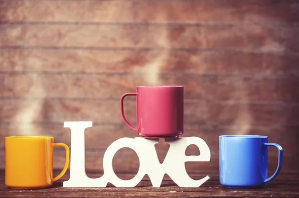 Tre koppar kaffe och ordet kärlek på träbord. Stockfoto