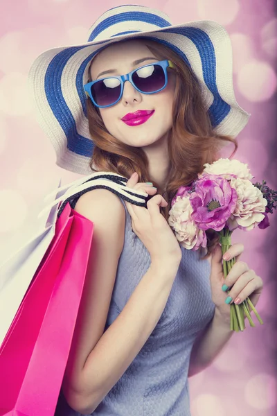 Redhead girl with shopping bags and flowers on pink background. — Stock Photo, Image