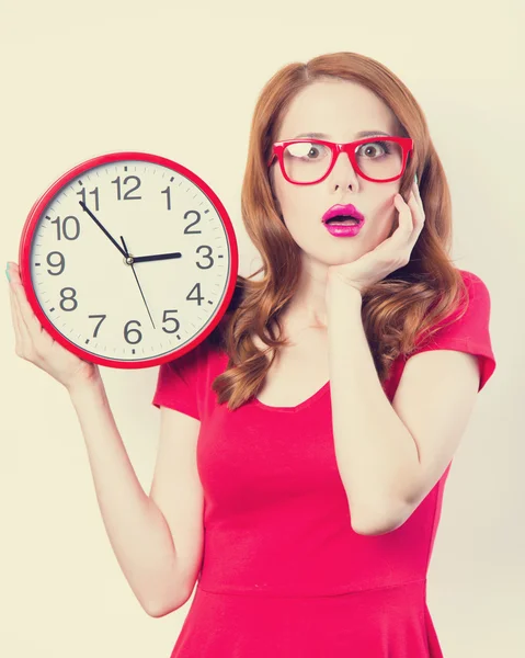 Surprised redhead girl with huge alarm clock on light background