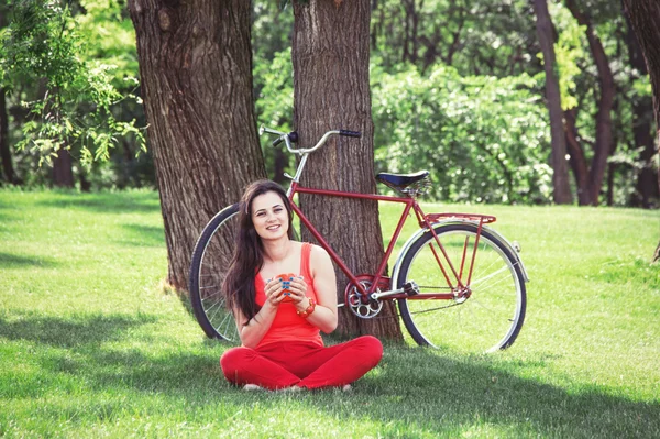 Brunette girl with cup of coffee in the park and with bicycle on — Stock Photo, Image