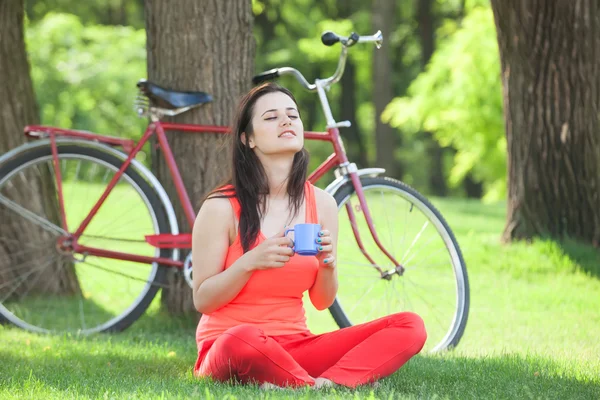 Chica morena con taza de café en el parque y con la bicicleta en — Foto de Stock