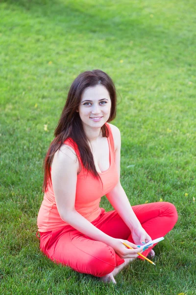 Menina morena com caderno sobre grama verde no parque . — Fotografia de Stock