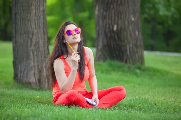Brunettee meisje met notitieblok op groen gras in het park. — Stockfoto