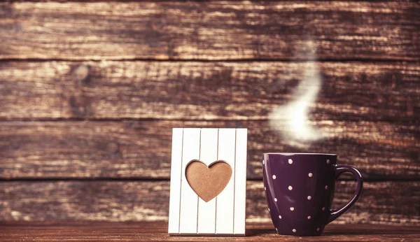 Marco con forma de corazón y taza de café sobre fondo de madera . — Foto de Stock