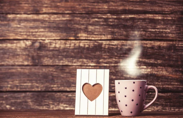 Marco con forma de corazón y taza de café sobre fondo de madera . —  Fotos de Stock