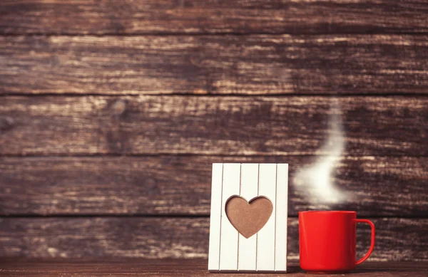 Каркас в форме сердца и чашка кофе на деревянном фоне . — стоковое фото
