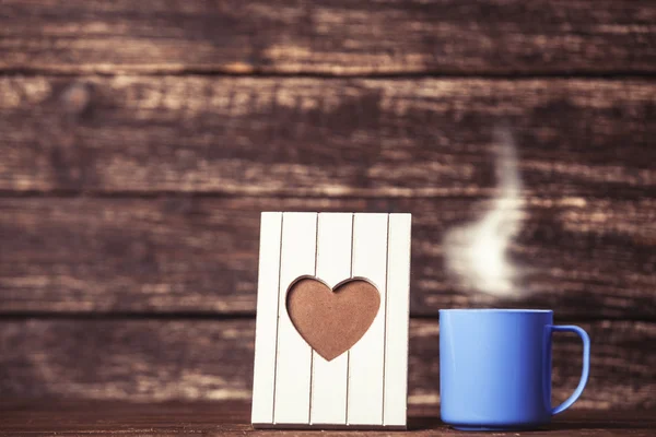 Frame with heart shape and cup of coffee on wooden background. — Stock Photo, Image