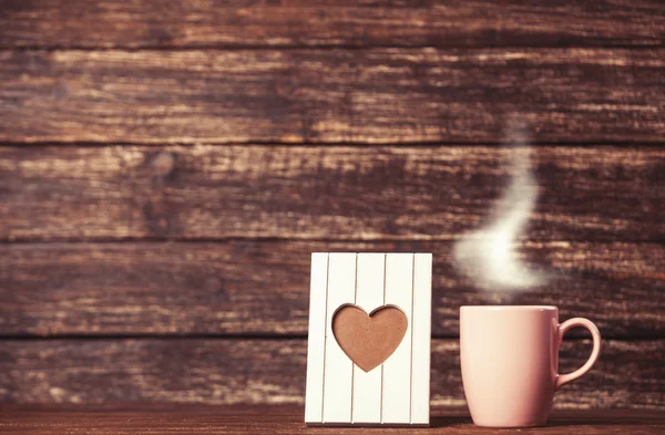 Frame with heart shape and cup of coffee on wooden background. — Stock Photo, Image