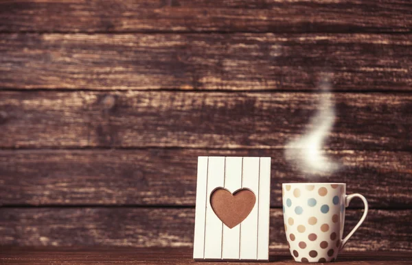 Telaio a forma di cuore e tazza di caffè su sfondo in legno . — Foto Stock