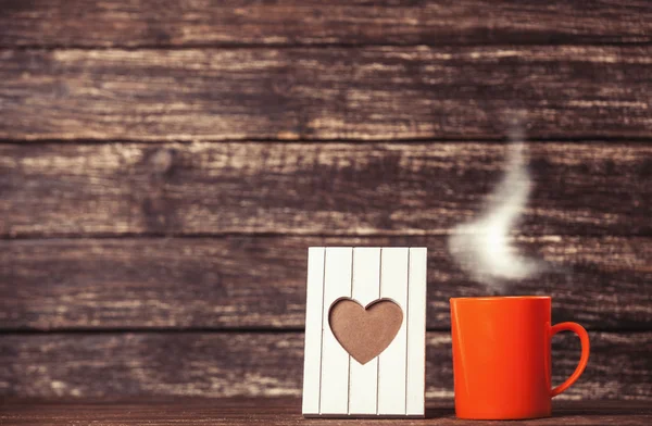 Frame with heart shape and cup of coffee on wooden background. — Stock Photo, Image