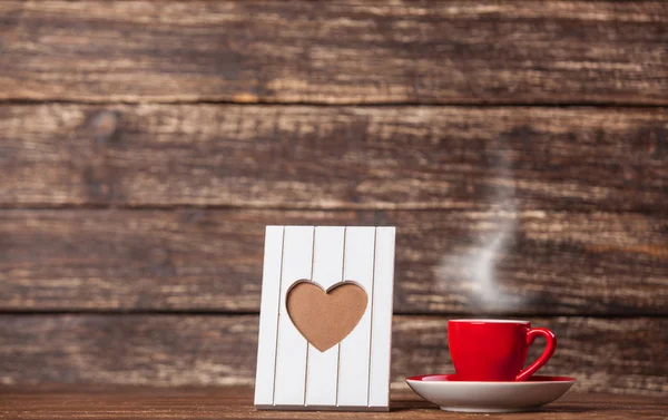 Marco con forma de corazón y taza de café sobre fondo de madera . — Foto de Stock