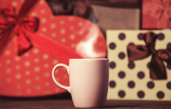 Cup of coffee and gifts on background. — Stock Photo, Image