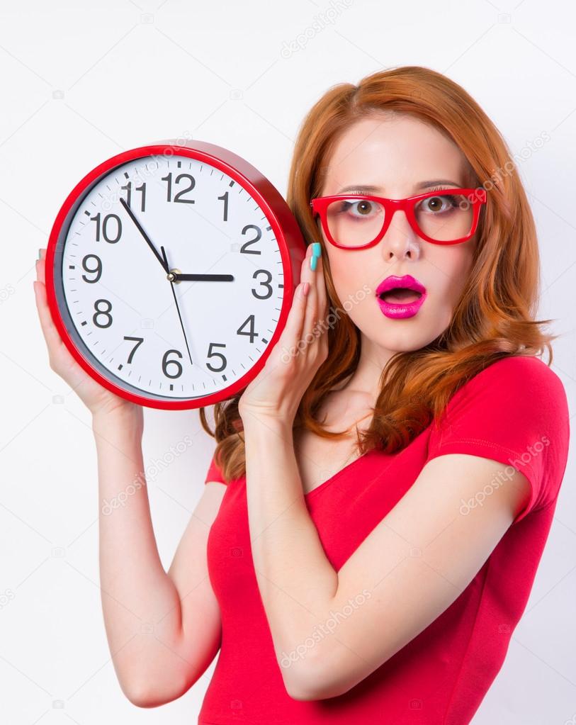 Surprised redhead girl with huge alarm clock on light background