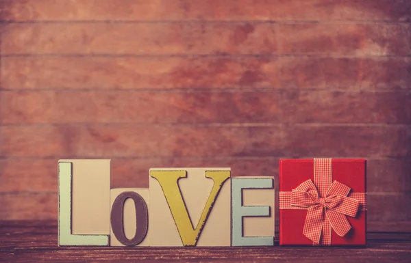 Pequeno presente e palavra Amor na mesa de madeira . — Fotografia de Stock