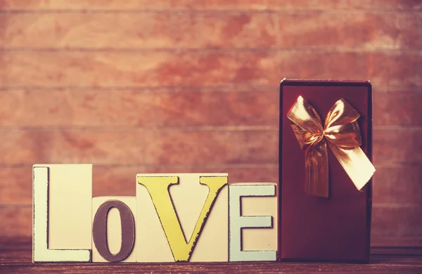 Pequeno presente e palavra Amor na mesa de madeira . — Fotografia de Stock