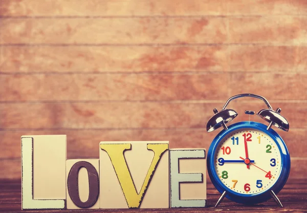 Reloj despertador y palabra Amor sobre mesa de madera . — Foto de Stock