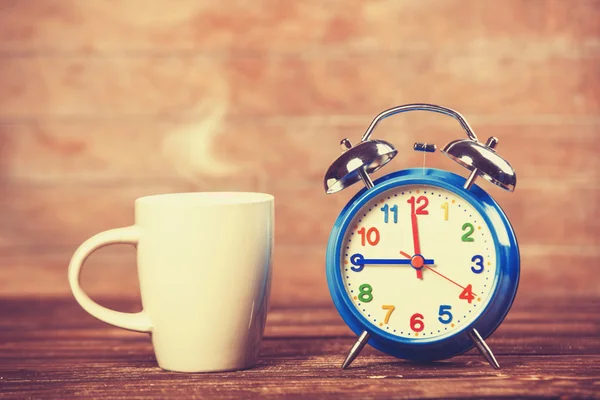 Cup of coffee and alarm clock on wooden table. — Stock Photo, Image