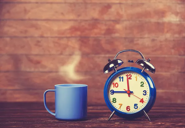 コーヒーのカップと木製のテーブルの上の目覚まし時計. — ストック写真