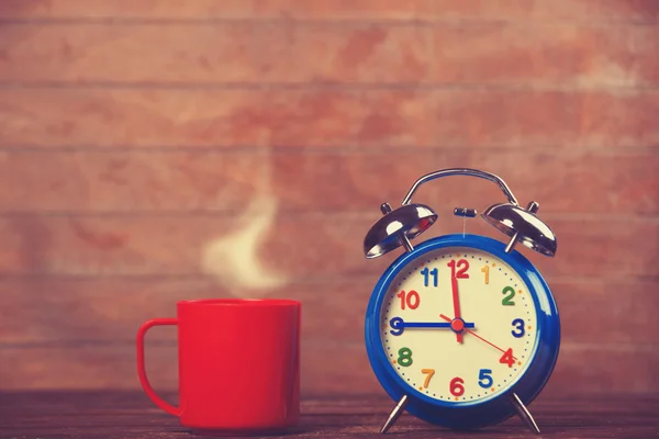コーヒーのカップと木製のテーブルの上の目覚まし時計. — ストック写真