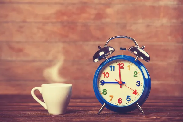 Cup of coffee and alarm clock on wooden table. — Stock Photo, Image