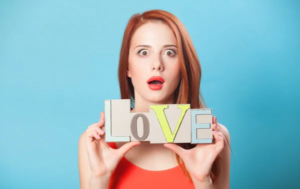 Überrascht rothaarige Frauen mit Wort Liebe auf blauem Hintergrund. — Stockfoto