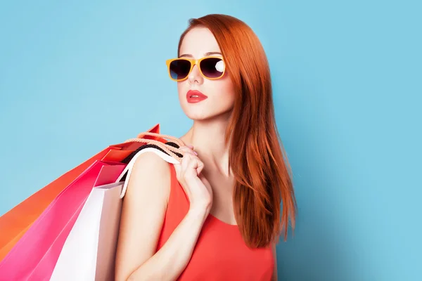 在蓝色背景上提着购物袋的风格红发女人. — 图库照片