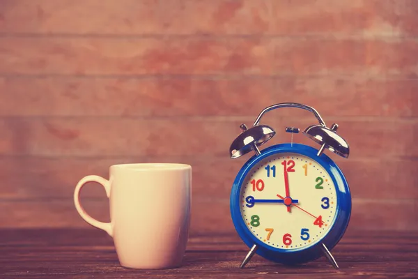 Cup of coffee and alarm clock on wooden table. Stock Image