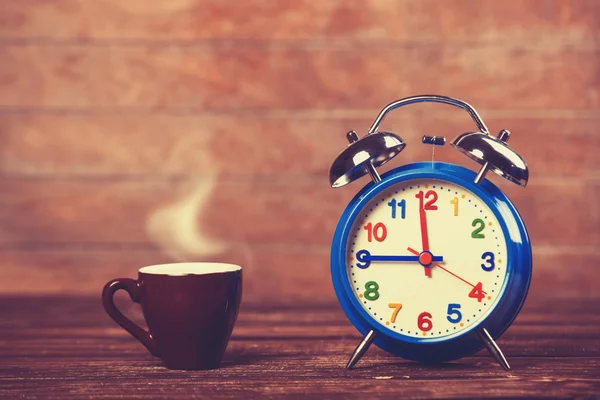 Cup of coffee and alarm clock on wooden table. Stock Photo