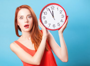 Kızıl saçlı kız büyük saatin üzerinde mavi arka plan ile.