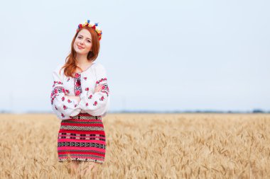 Redhead girl in national ukrainian clothes on the wheat field. clipart