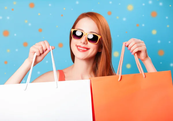 Estilo mujer pelirroja sosteniendo bolsas de compras sobre fondo azul . —  Fotos de Stock