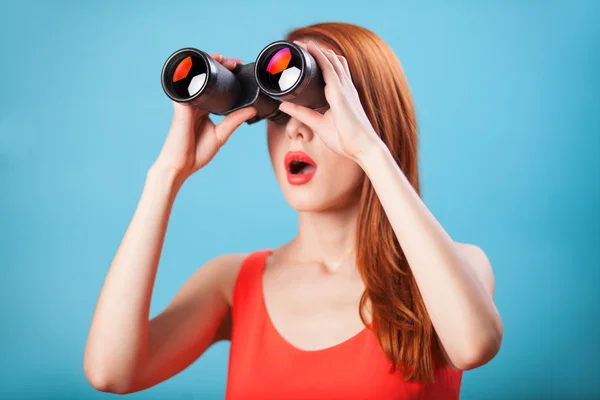 Menina ruiva com binocular no fundo azul . — Fotografia de Stock