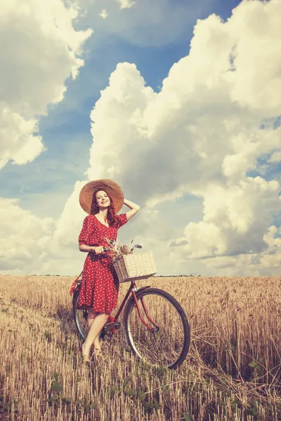 Redhead boerenmeisje met fiets op tarweveld. — Stockfoto