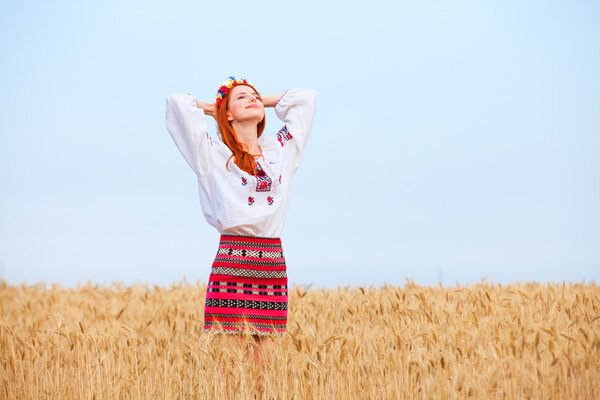 Redhead girl in national ukrainian clothes on the wheat field.
