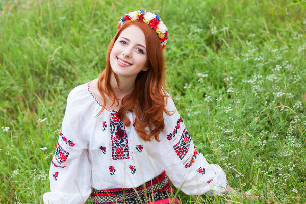 Redhead girl in nationac ukrainian clothes on the green grass.